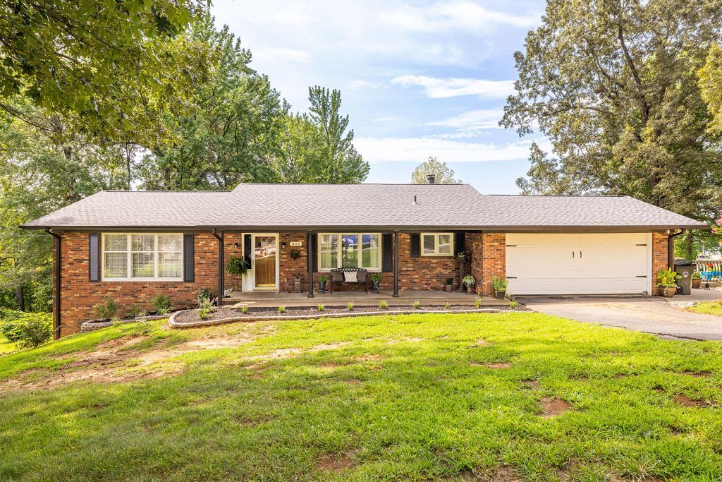 Single-story brick ranch house with a two-car garage, front lawn, and trees in daylight