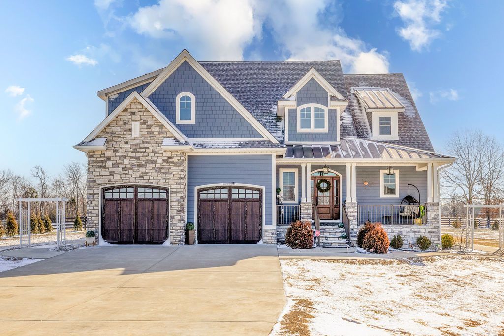 Snowy suburban house with blue-gray siding, stone facade, and three garage doors under a clear sky