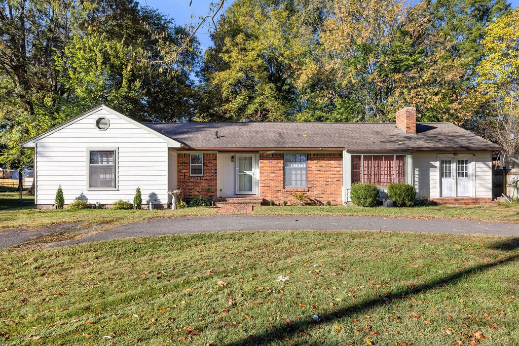 Single-story brick-and-white house with a front lawn and trees in autumn sunlight