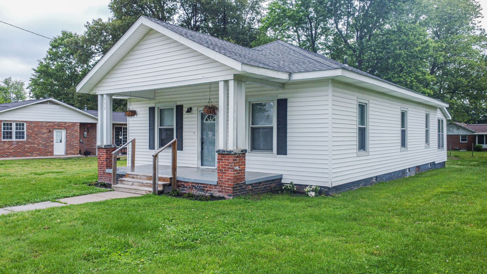 Small white single-story house with a front porch, red brick steps, and green lawn.