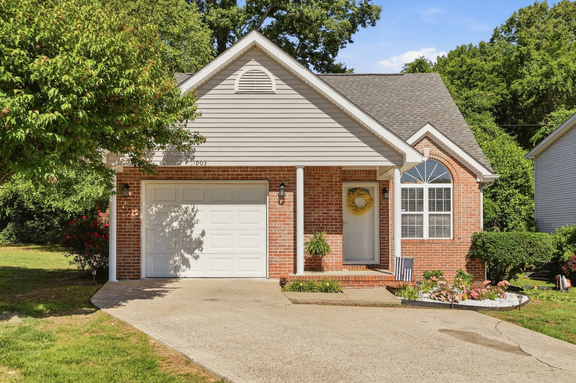 Suburban brick house with a white garage door, front porch, and landscaped yard in daylight