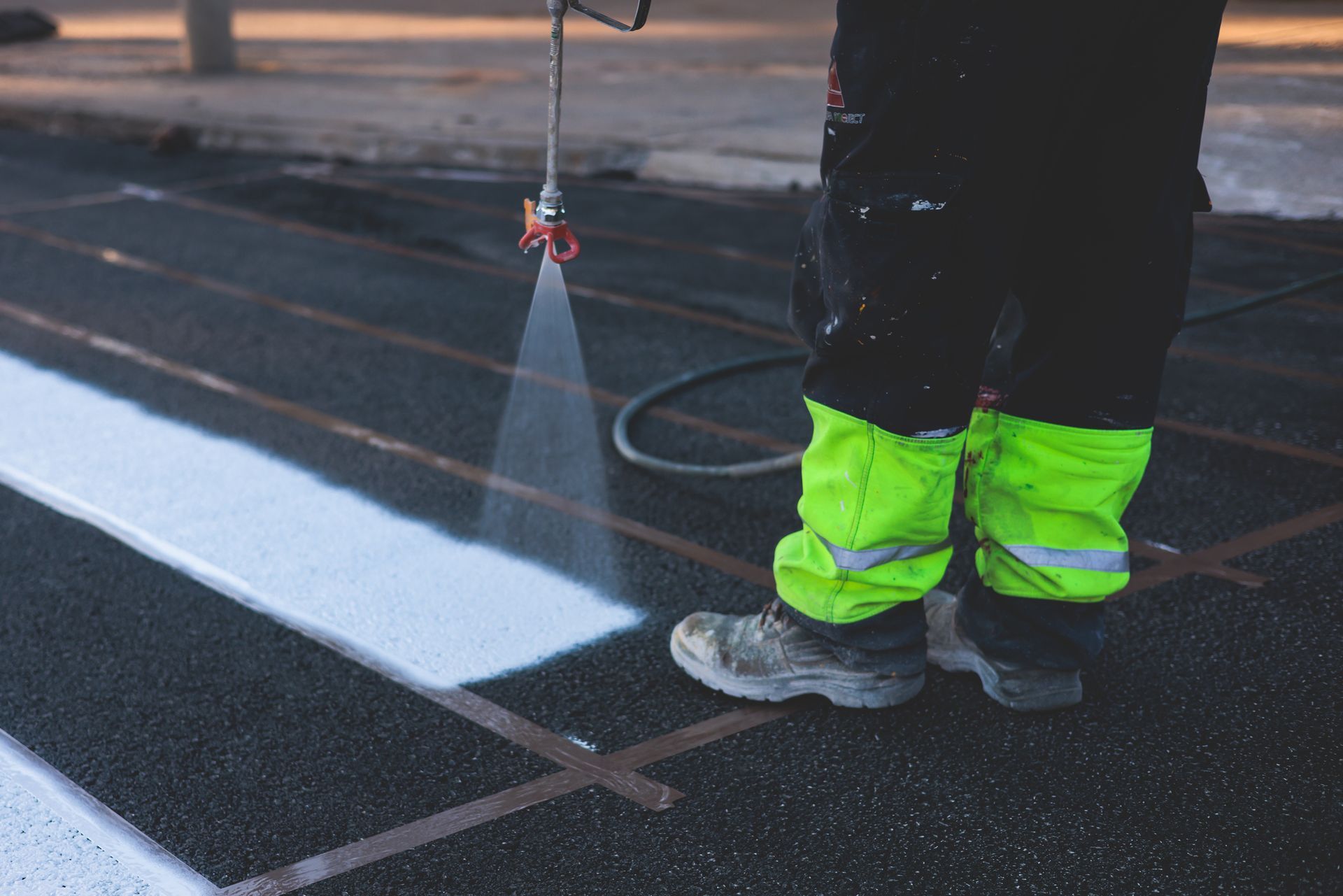 Person in safety gear spraying white paint onto pavement, creating a crosswalk.