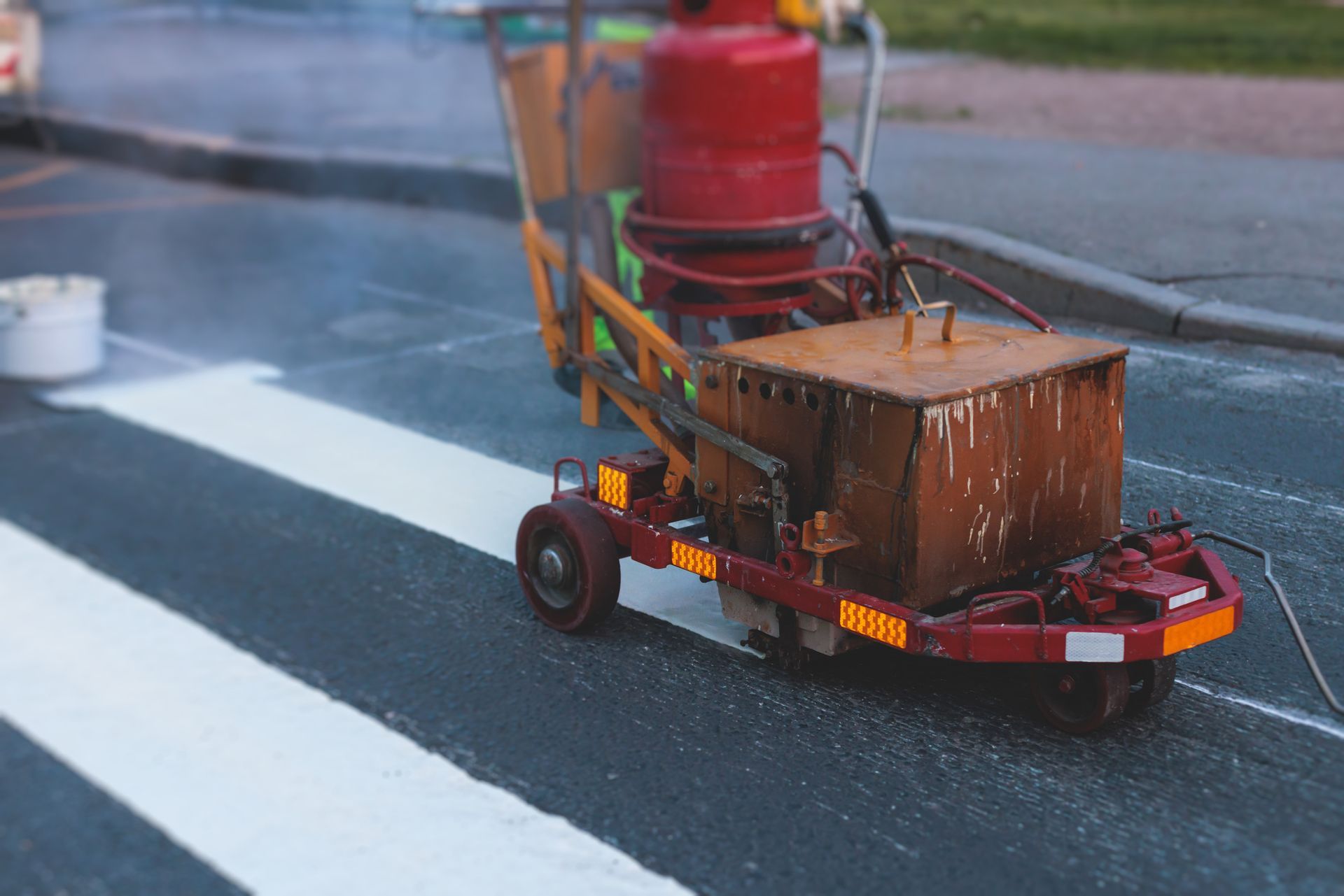 Road marking machine painting a white crosswalk on asphalt.