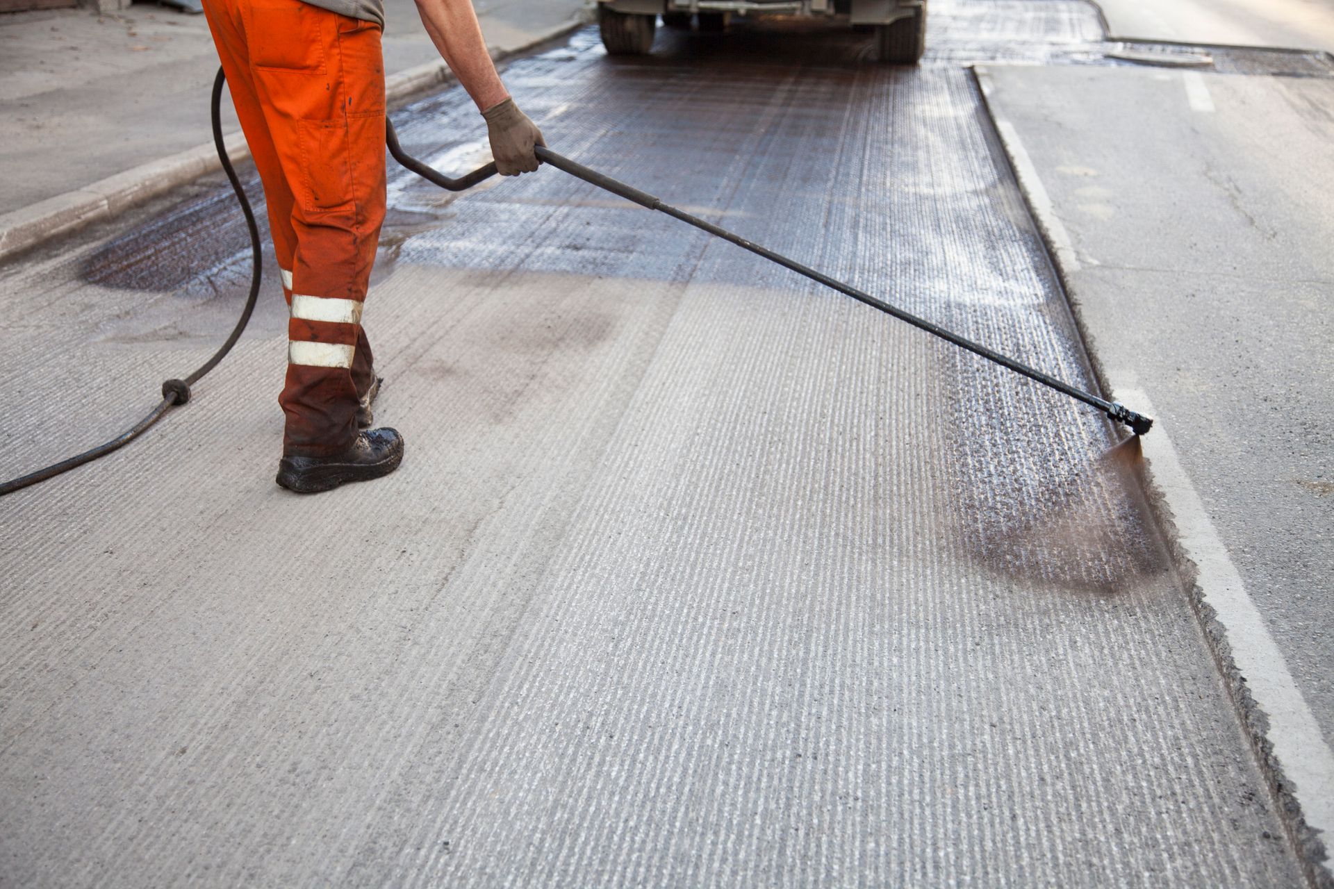 Worker spraying asphalt sealant on road.
