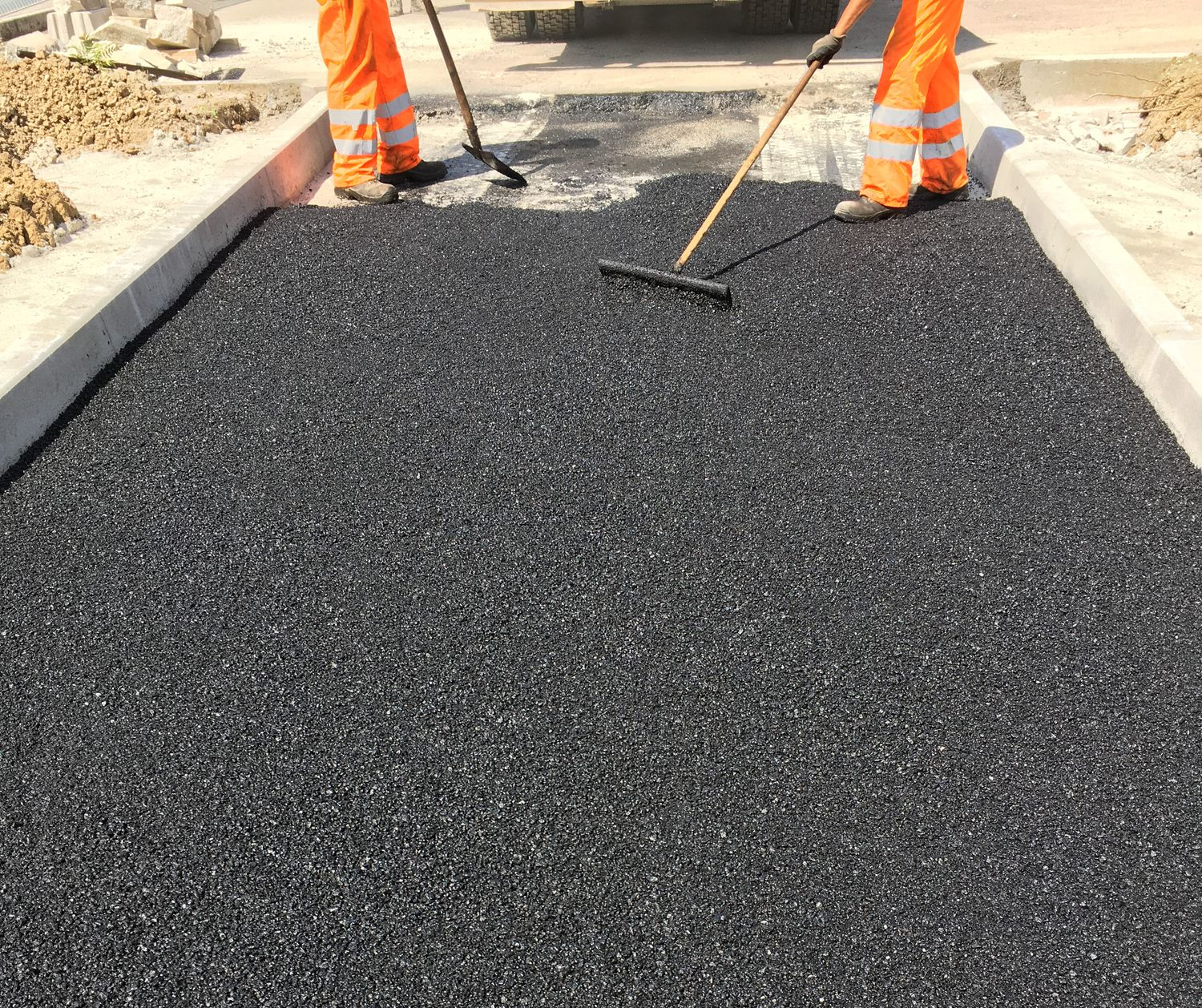 Workers in orange coveralls spread fresh asphalt on a road. Workers in orange coveralls spread fresh asphalt on a road.