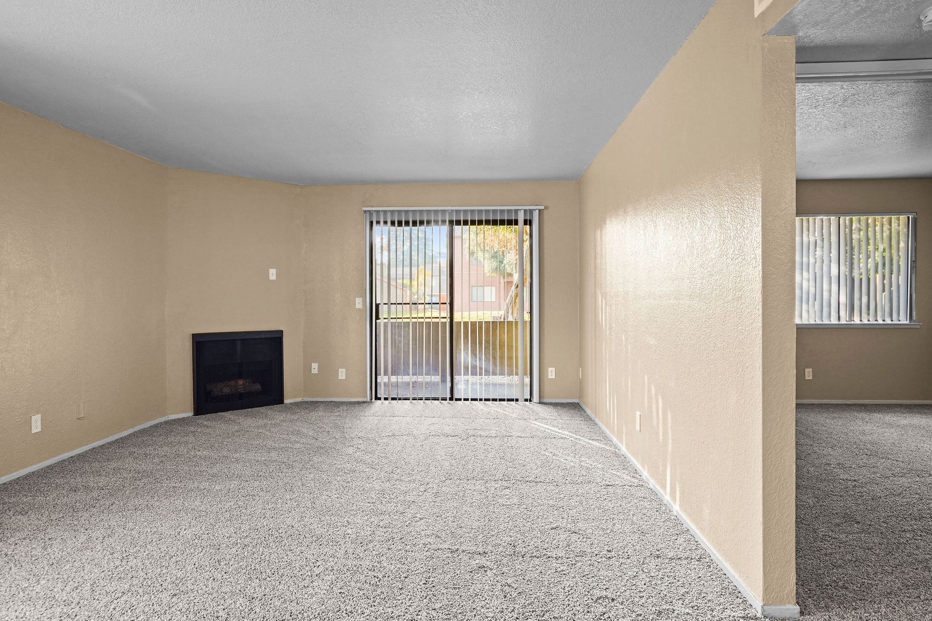 Empty beige living room with carpet, fireplace, and sliding glass doors.