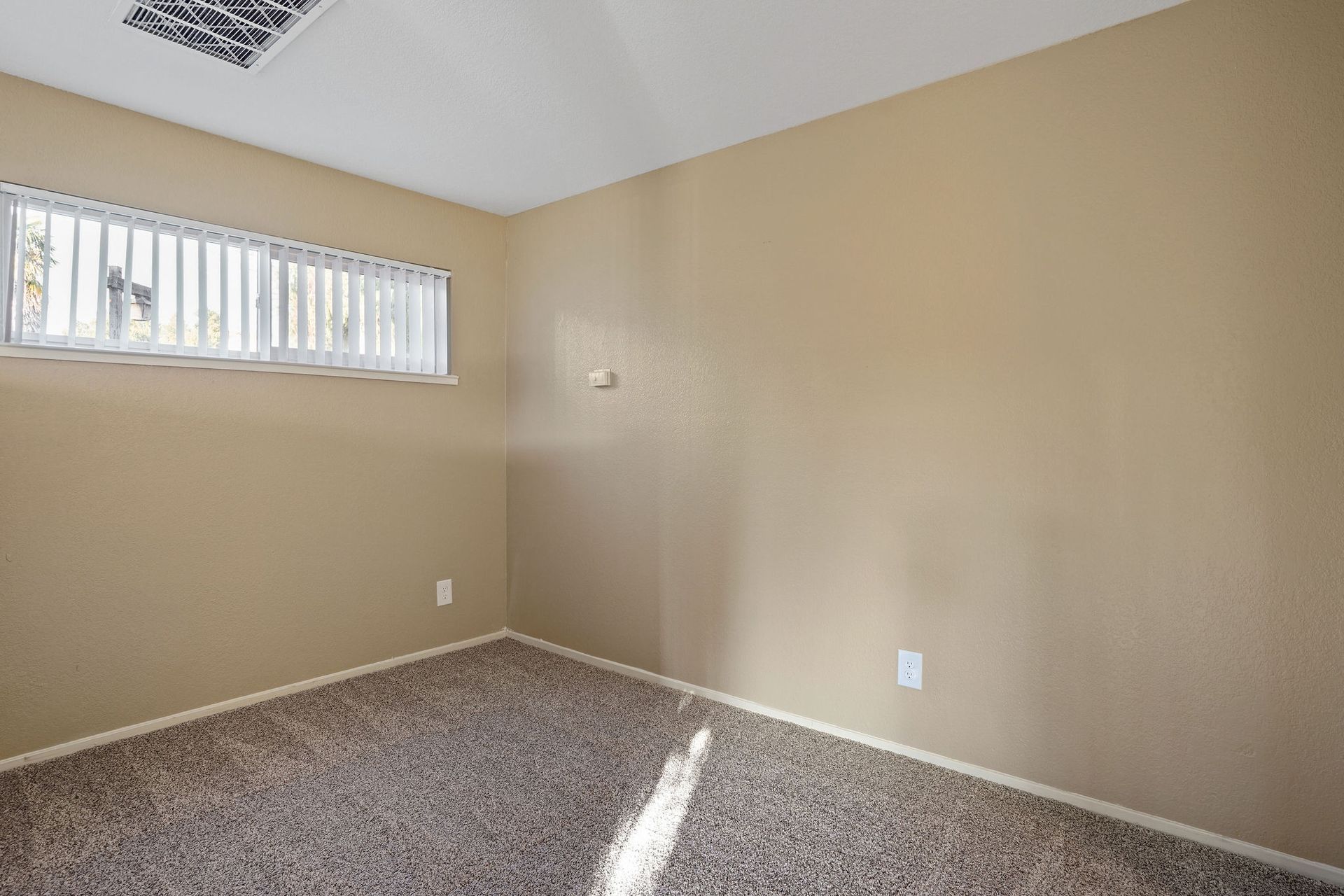 Empty beige carpeted room with a small high window and white ceiling.