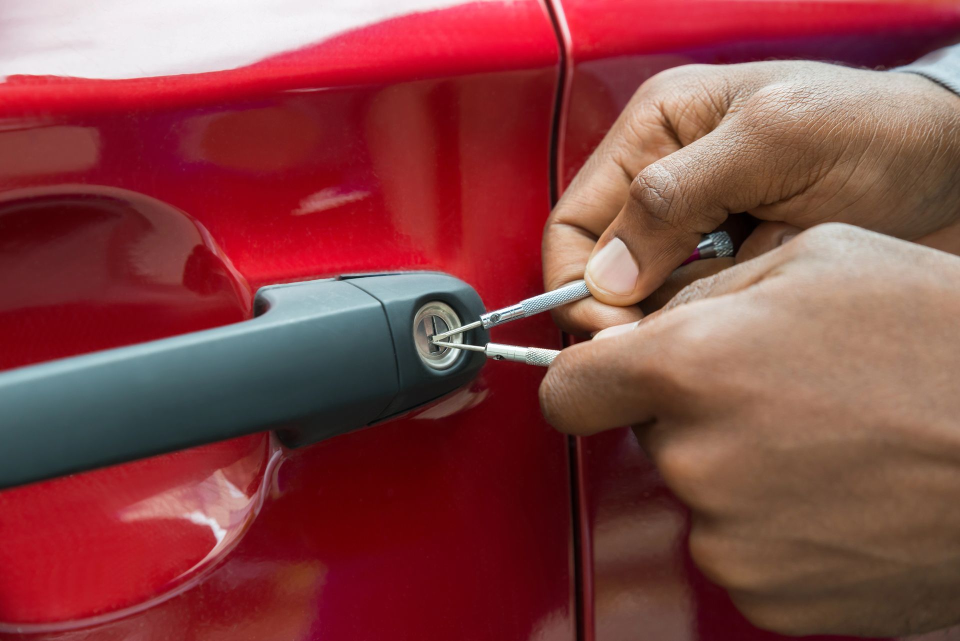 Manos usando una llave para abrir la puerta de un coche rojo.