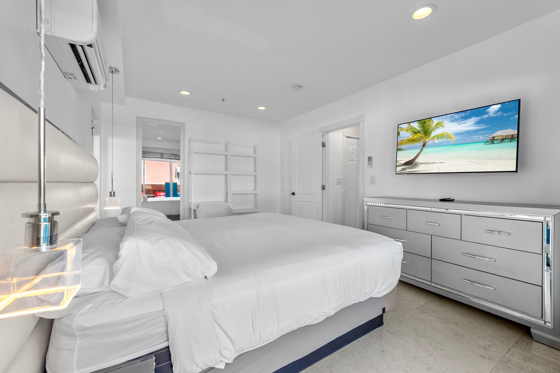 White bedroom with king bed, TV, dresser, and air conditioner.