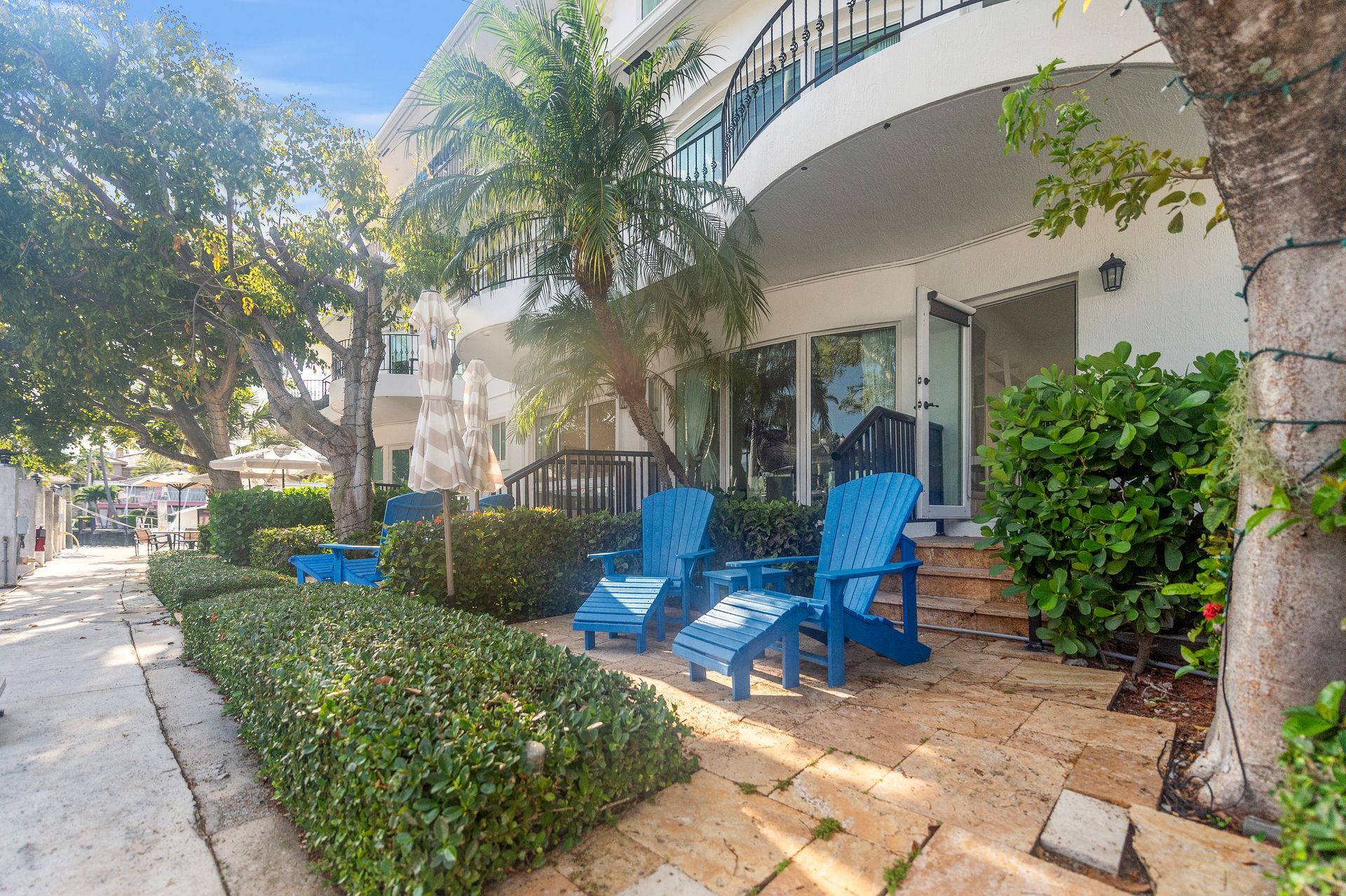 Exterior view of a building with blue chairs on a patio, bordered by greenery.