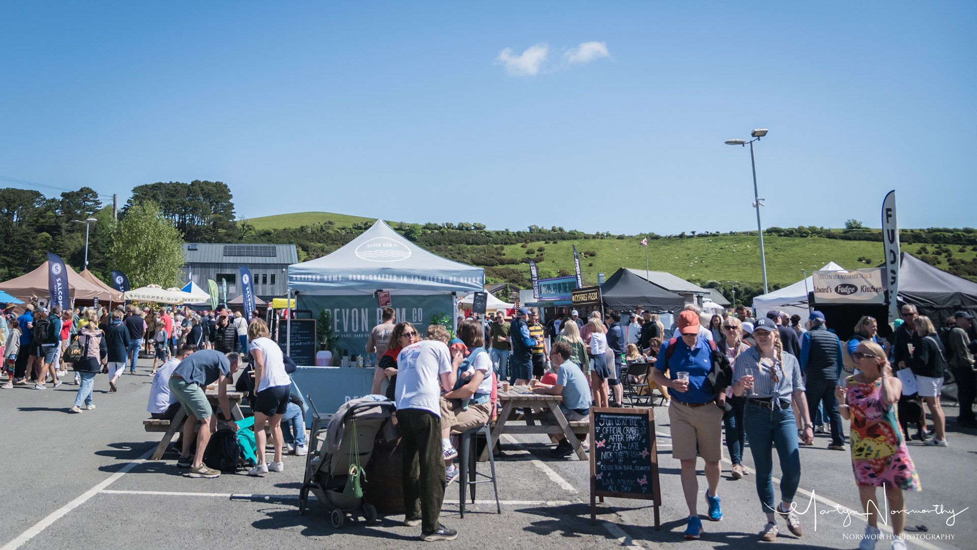 Outdoor market with many people, tents, and blue sky.