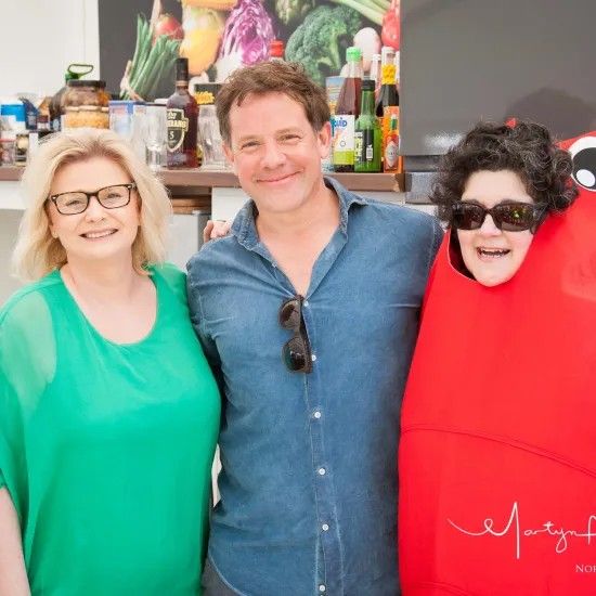 Three people smiling together: A woman in green, a man in denim, and a person in a red lobster costume.