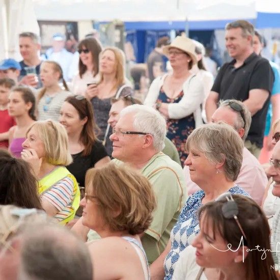 Crowd of people watching an event outdoors, with various expressions and attire.