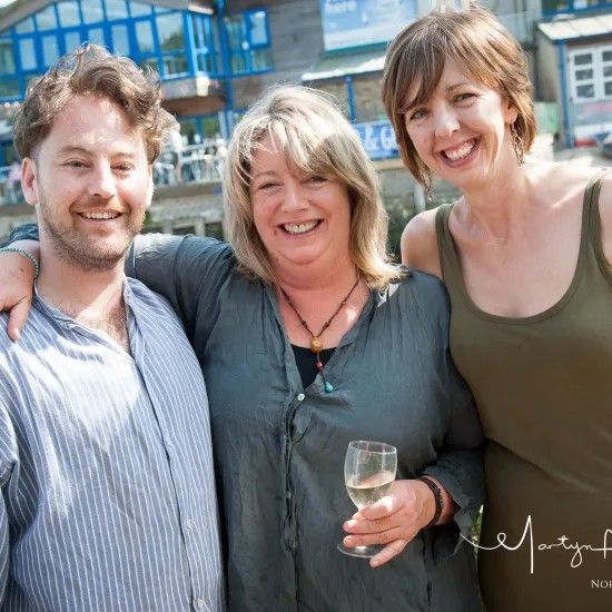 Three smiling people outdoors, one holding a drink, two with arms around each other.