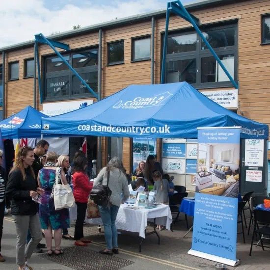 People at a Coast & Country real estate booth, blue tent, outside a modern building.