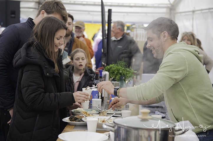 Man serving food to a woman at an outdoor event; others watch.