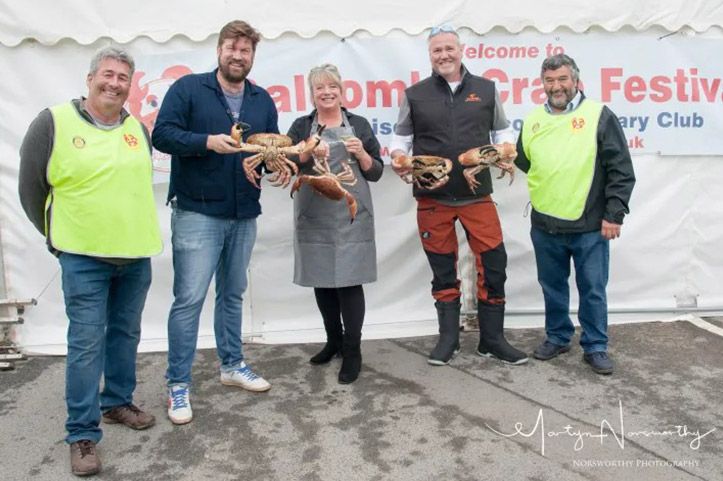 Five people holding crabs at the Salcombe Crab Festival. Outdoors with a white tent in the background.