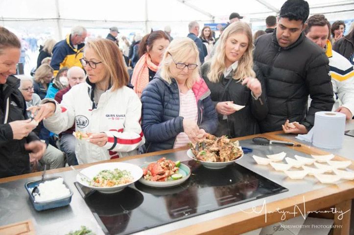 People sampling food at a gathering, standing around a counter with dishes.