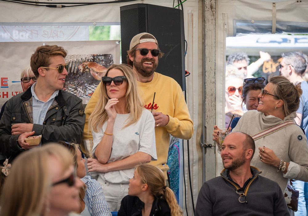 People at an outdoor event, some wearing sunglasses. A man in yellow sweatshirt is in the center.