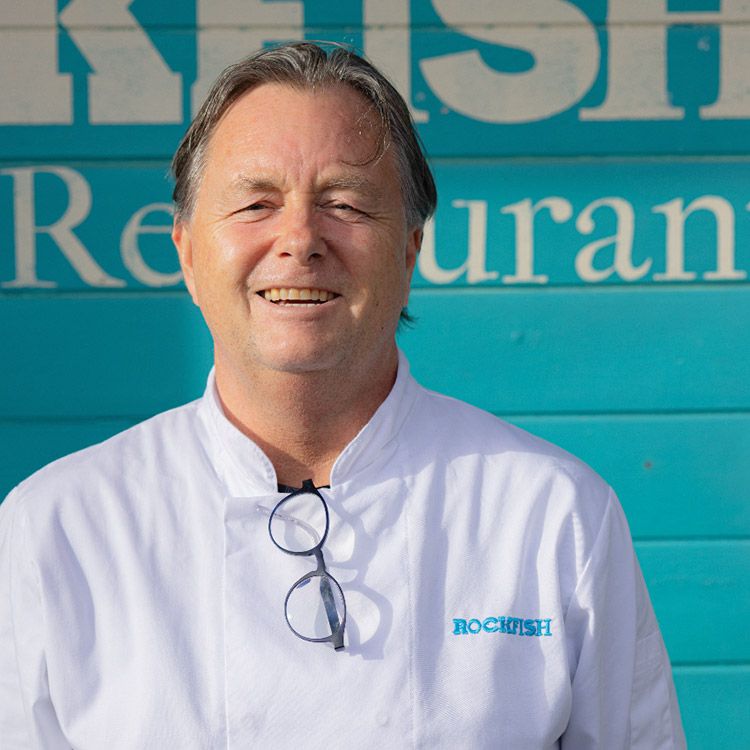 Chef smiling in white coat, in front of