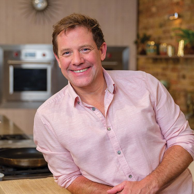 Man in pink shirt smiling in kitchen; stove, oven, and counter visible.
