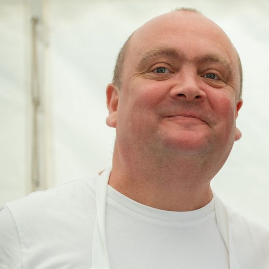Man with a shaved head and a smile wearing a white shirt and apron.