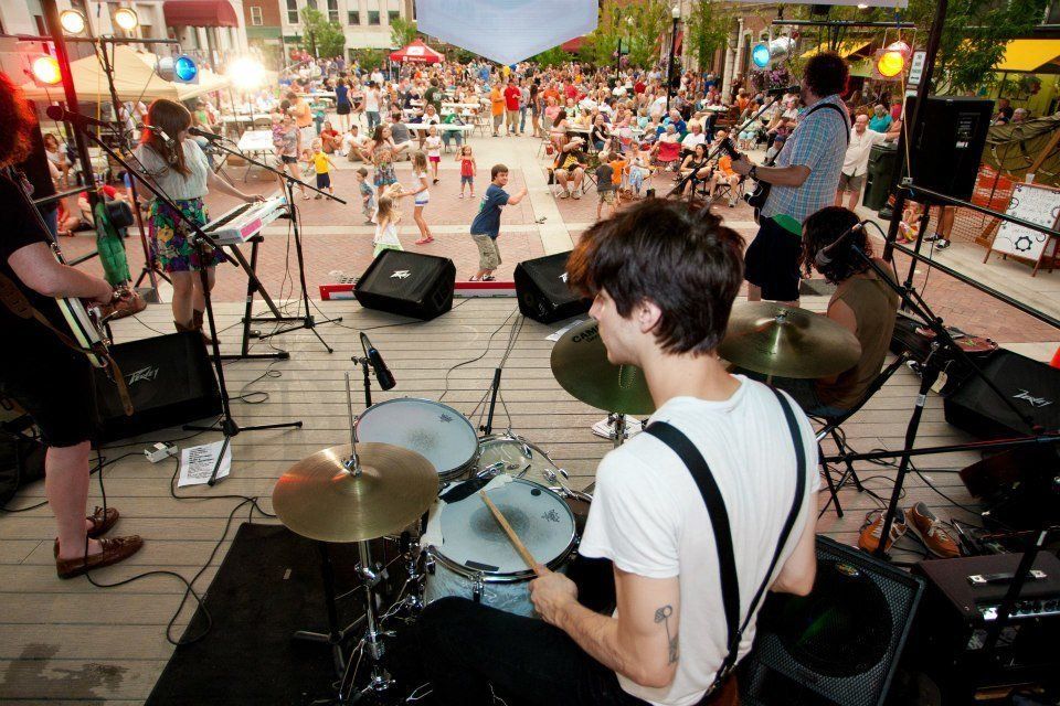 A man is playing drums on a stage in front of a crowd in Sumner County Gallatin TN square.
