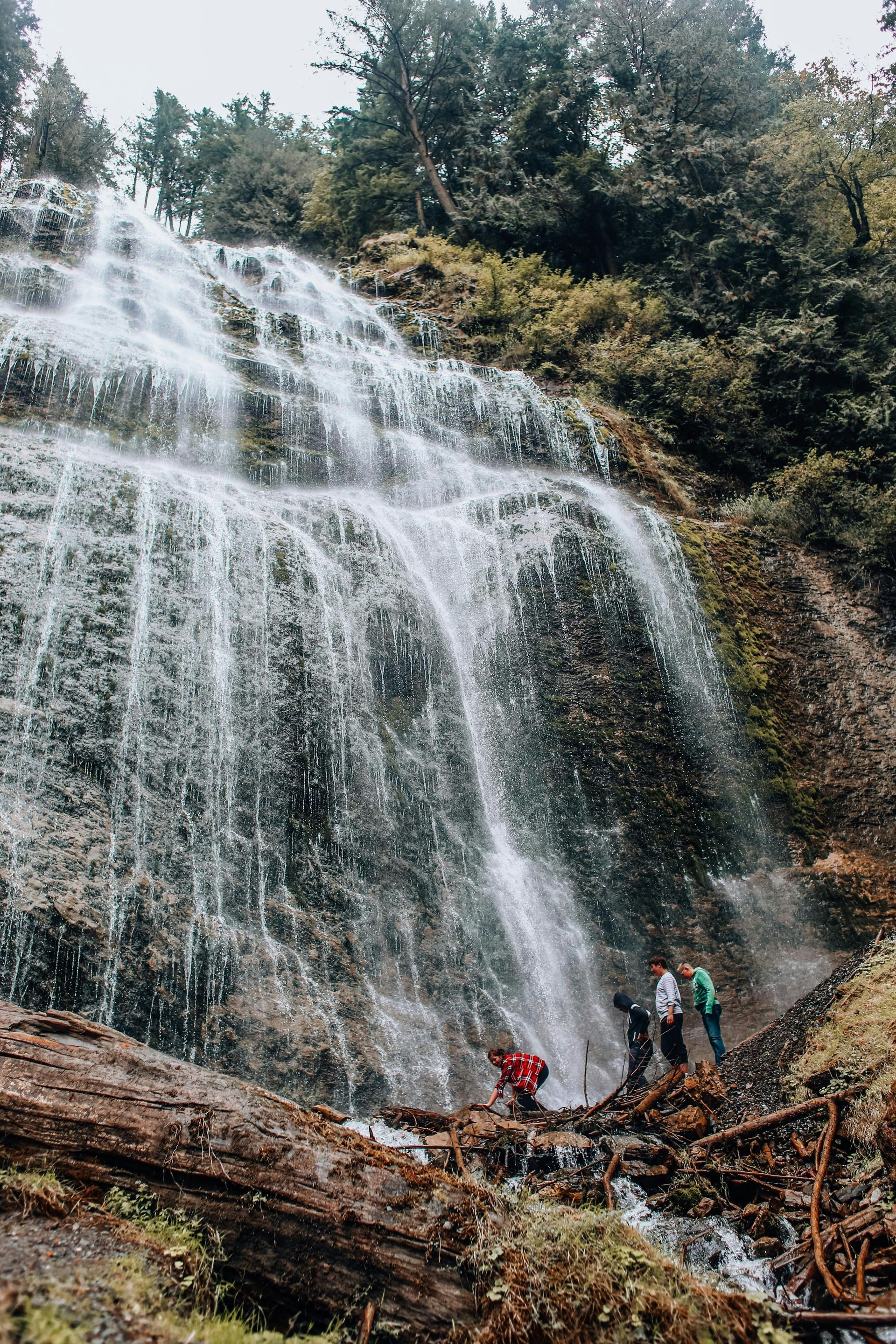 A group of people are standing in front of a waterfall.
