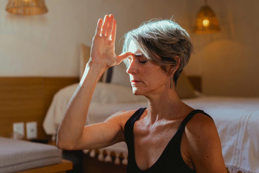 A woman is sitting on a bed with her hand on her nose.
