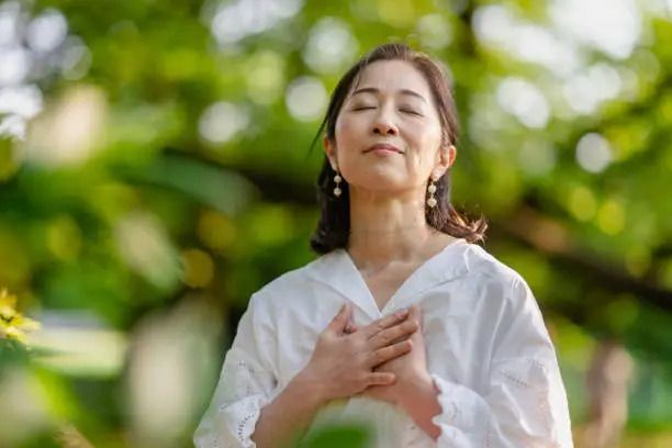 A woman is standing with her eyes closed and her hands on her chest.