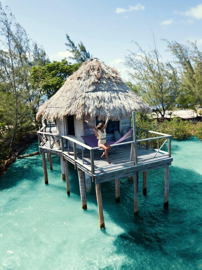 Thatched overwater bungalow on turquoise water with a person relaxing on the deck