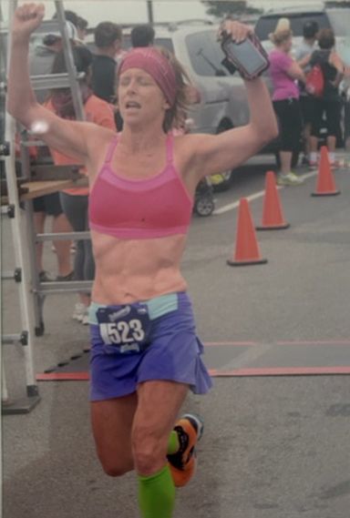 A woman in a pink top and purple shorts has the number 5223 on her belt