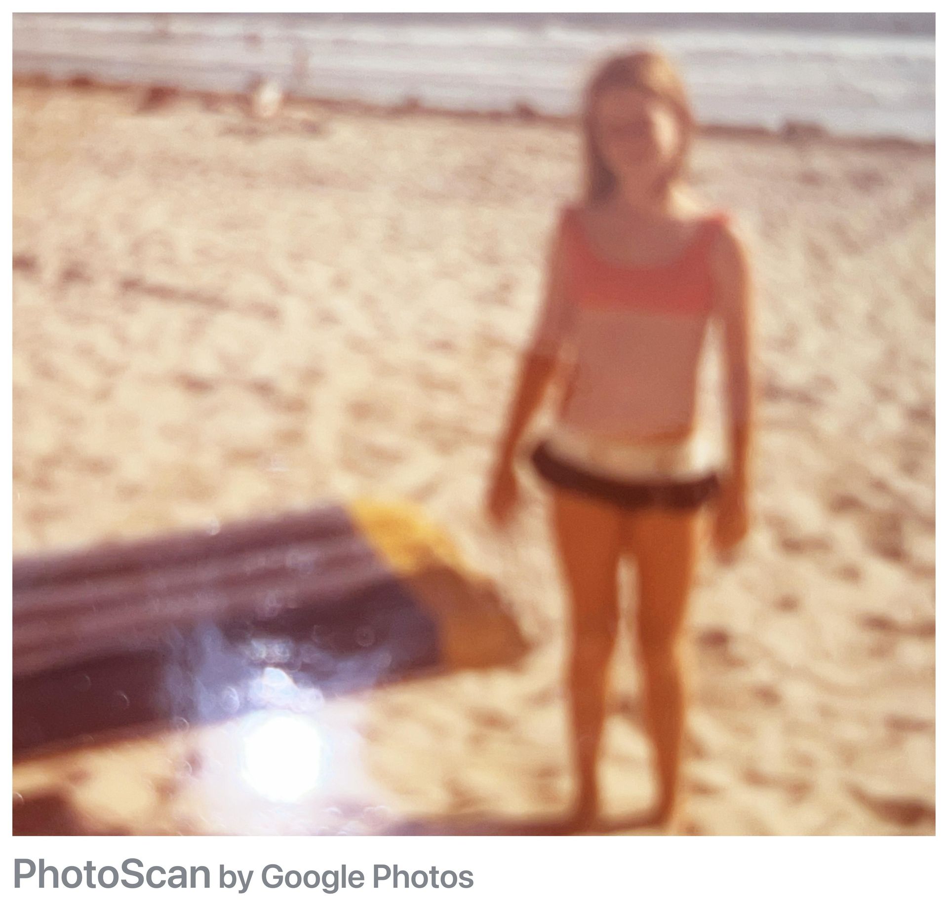 Girl in bathing suit stands on beach, surfboard nearby.