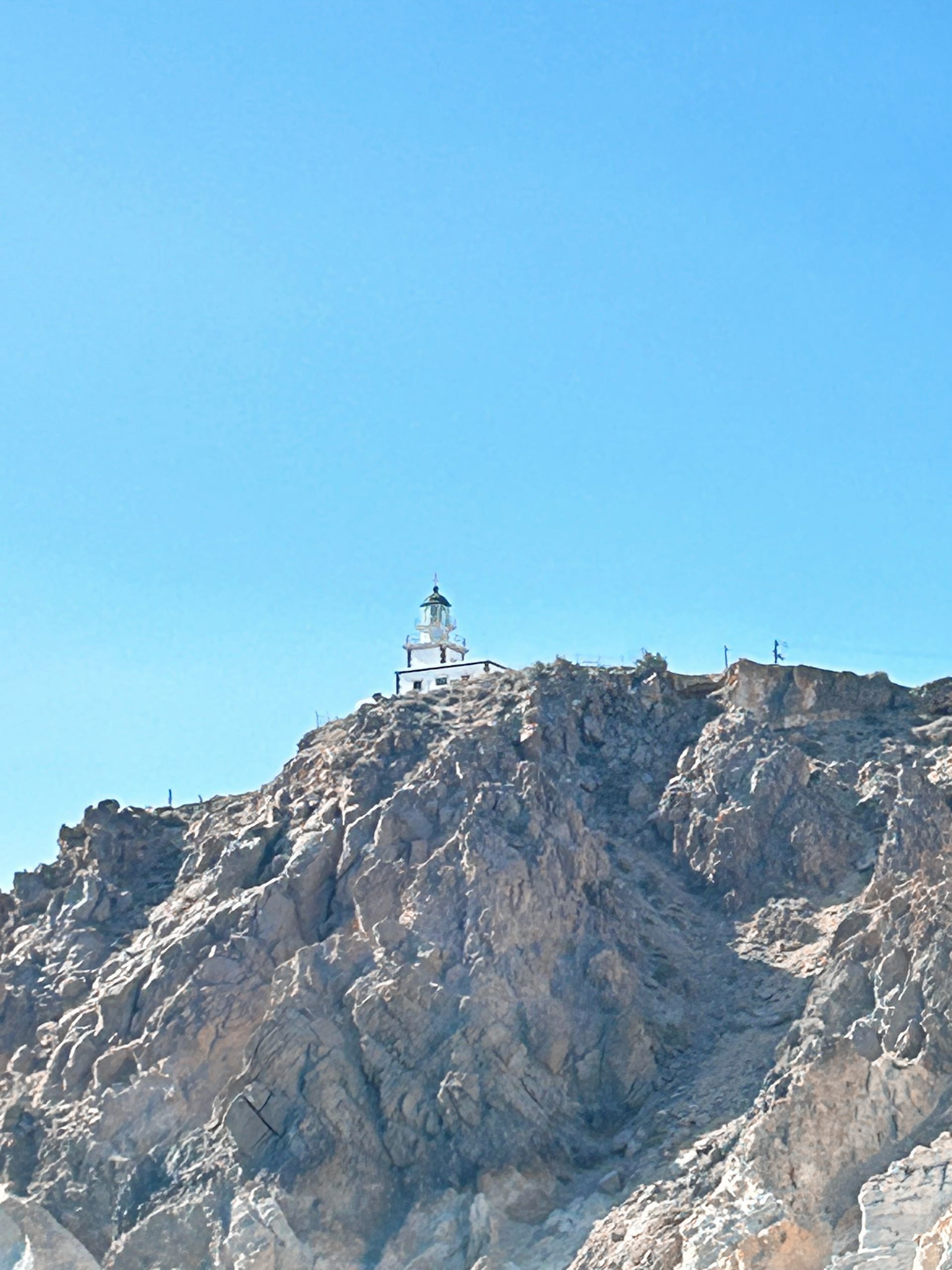 Lighthouse on a rocky mountaintop against a clear blue sky.