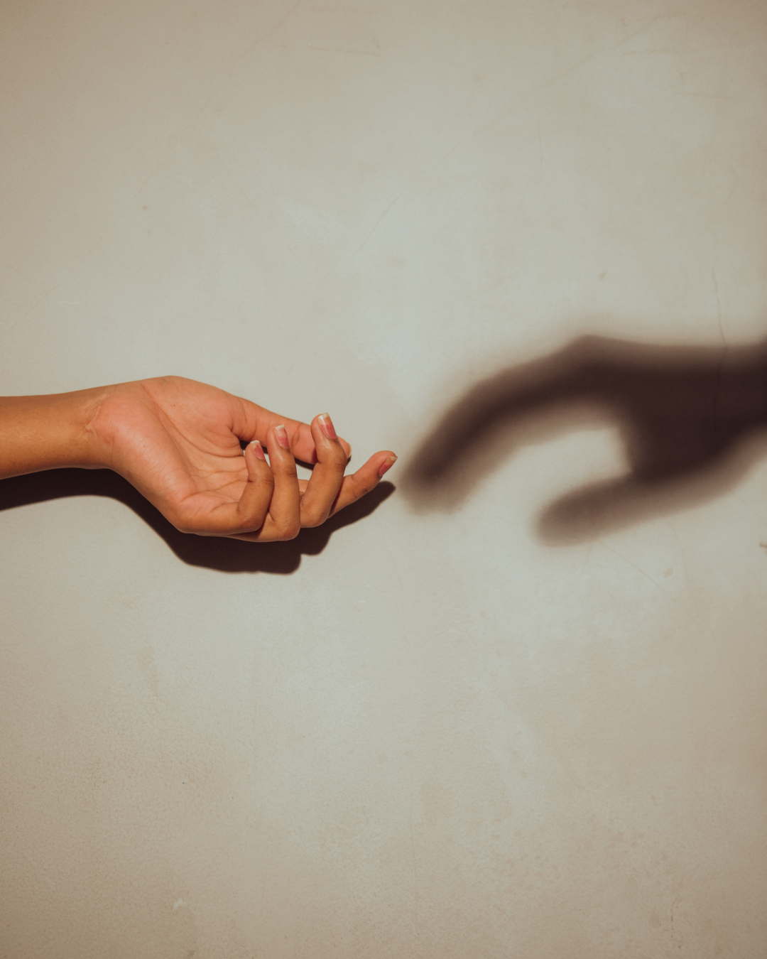 Hand reaching towards its shadow on a light blue wall.