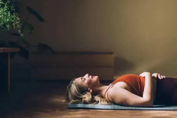 Woman lying on a yoga mat in a calm indoor pose, lit by soft natural light