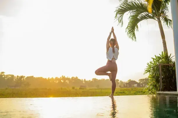 Woman in tree pose by a pool at sunrise.