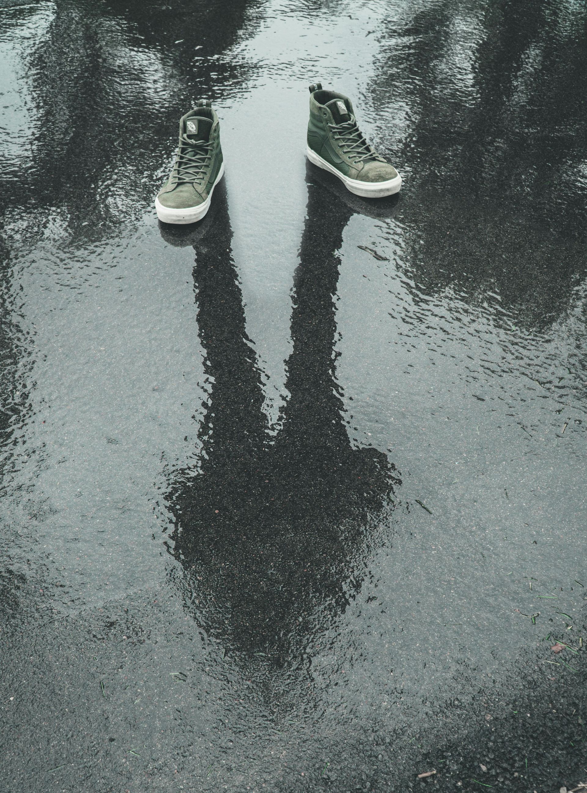Shadow of person standing in puddle; green high-top sneakers visible.