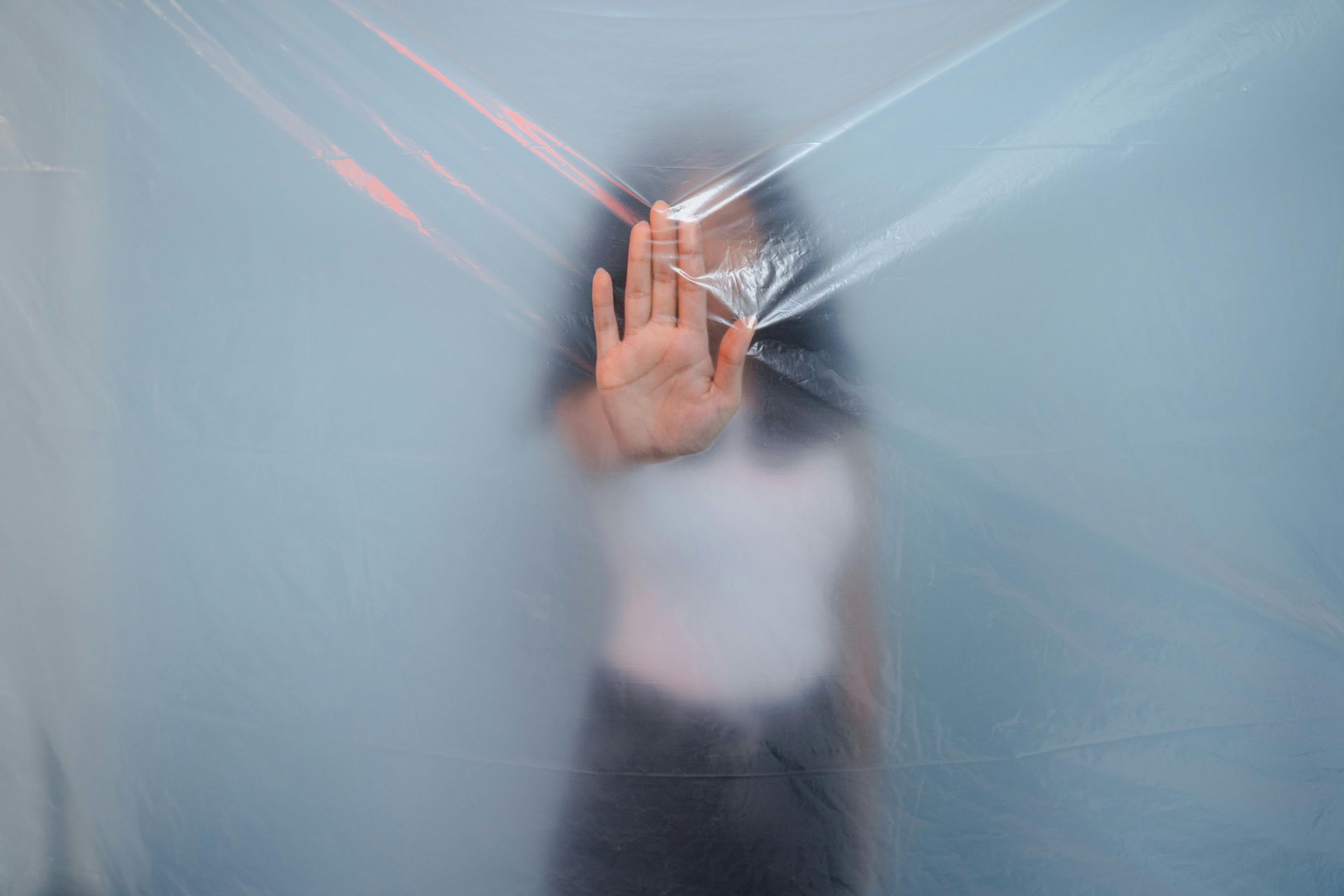 Hand pressed against frosted glass with cracks, blurred figure behind it
