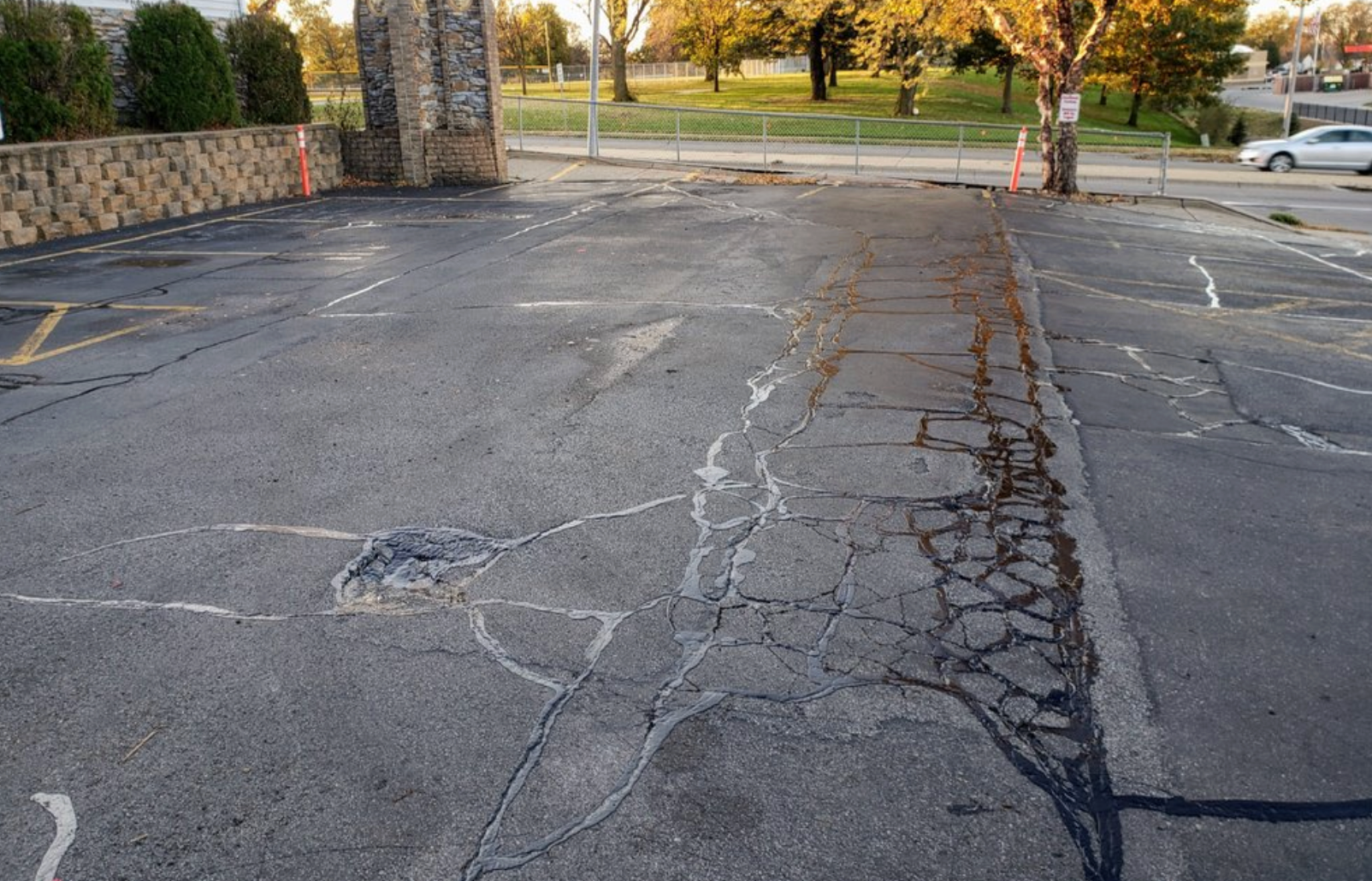 Worker applying sealant to asphalt pavement with a long-handled squeegee.