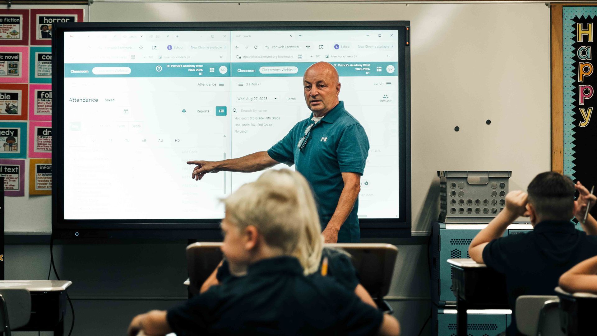 Teacher pointing at a screen in a classroom, students in foreground.