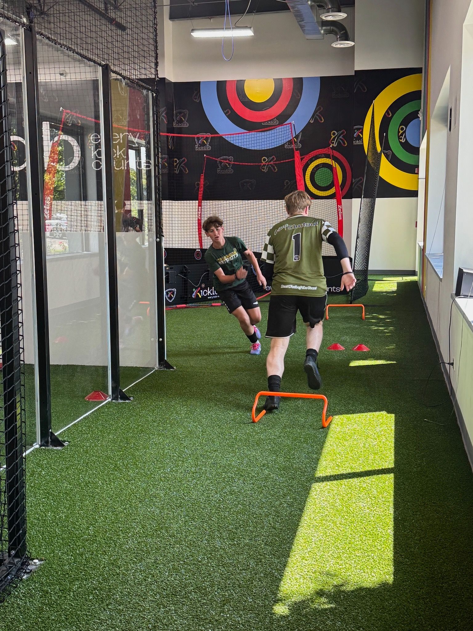 Two people training on indoor turf with colorful target rings on the wall