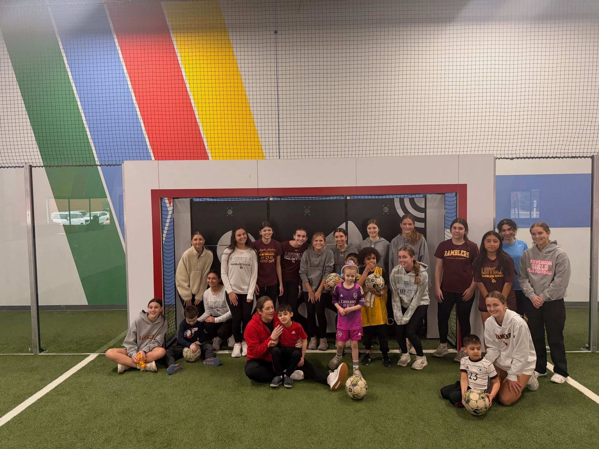 Group of people posing on an indoor soccer field in front of a goal and colorful wall panels