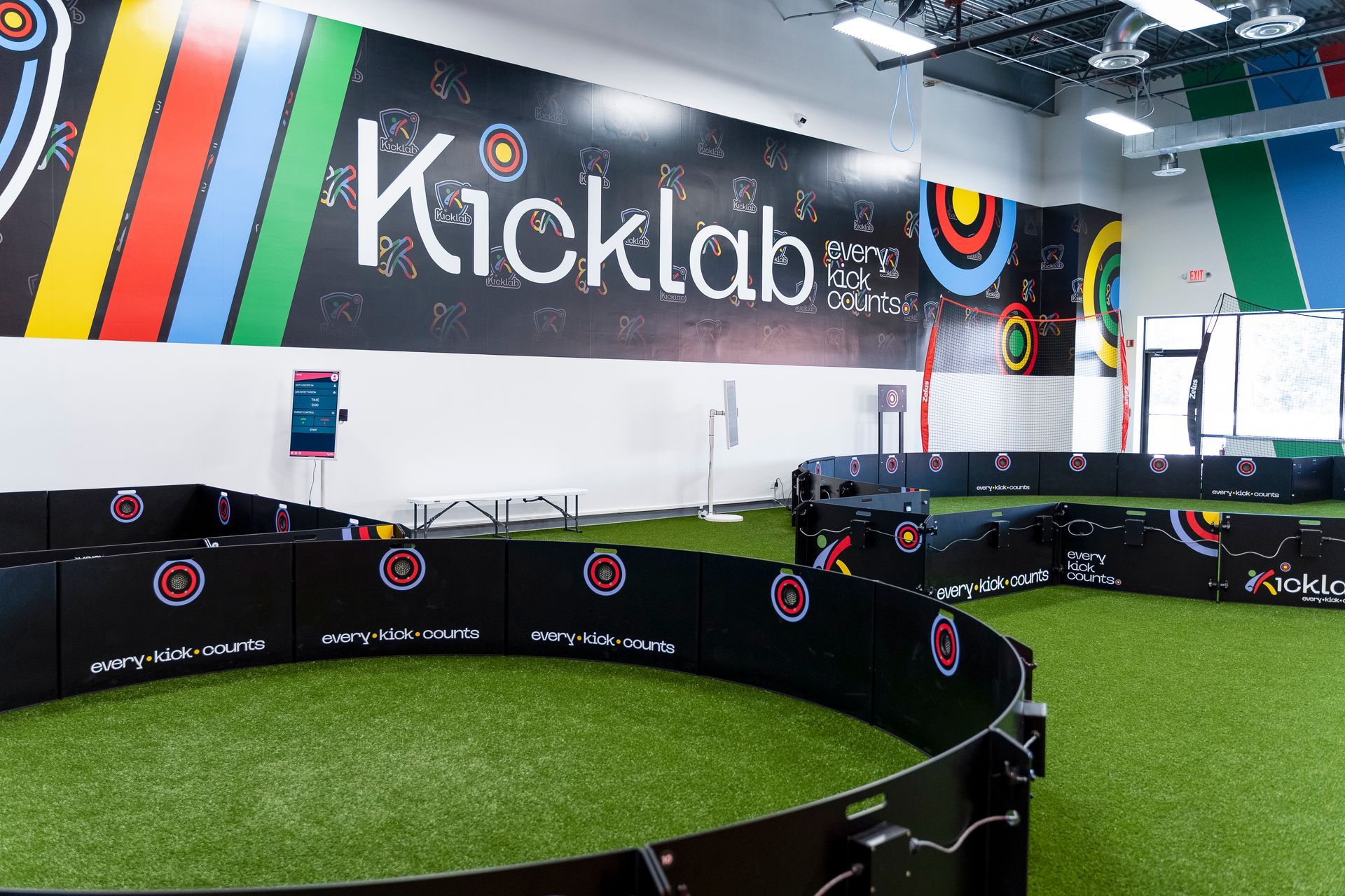 Kicklab indoor soccer court with green turf, black boards, and colorful wall graphics