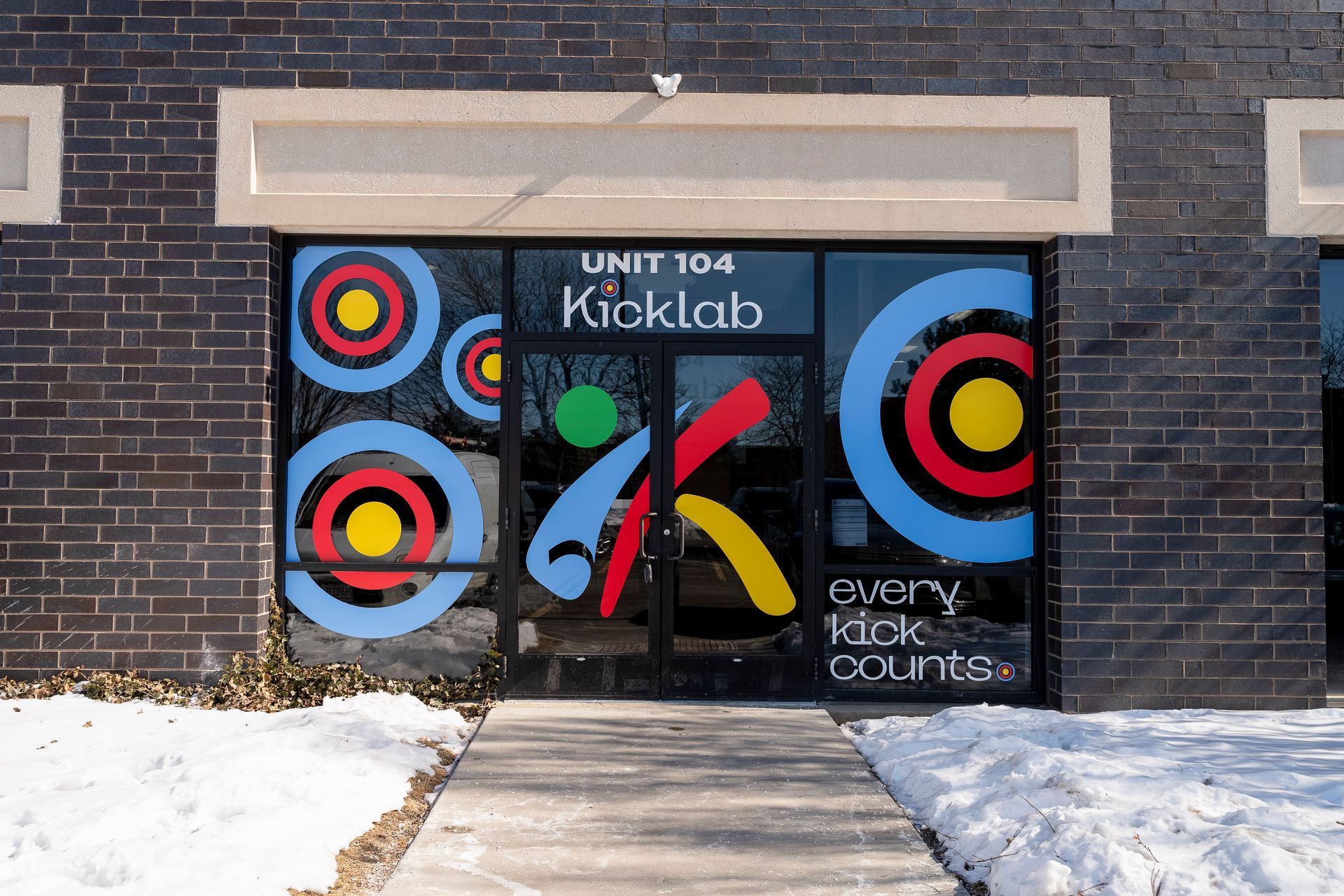Colorful storefront mural for Unit 104 Kiokab, with bright circular designs and snowy walkway.