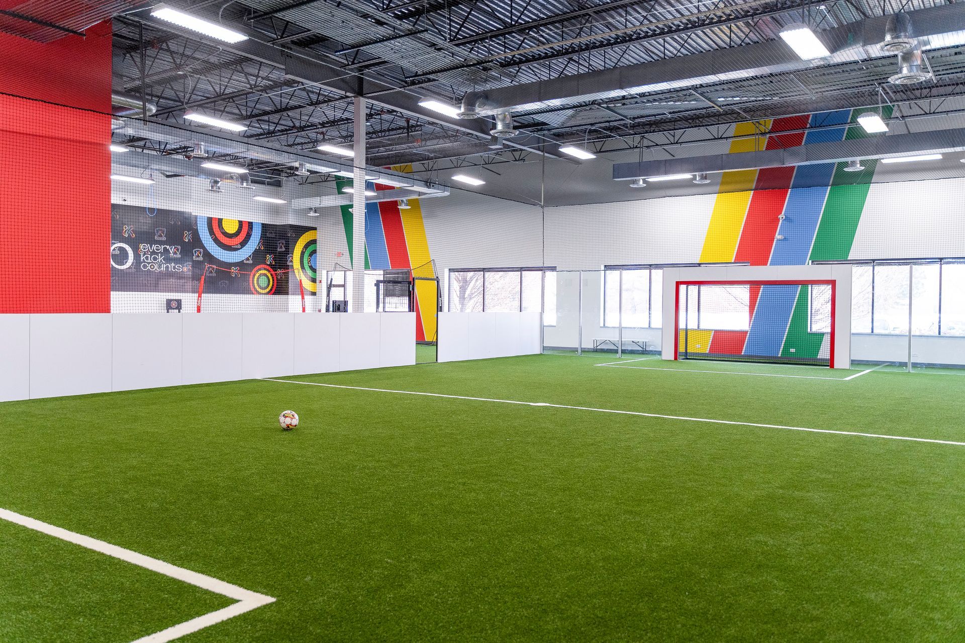 Indoor soccer field with green turf, colorful wall murals, and a goal near large windows