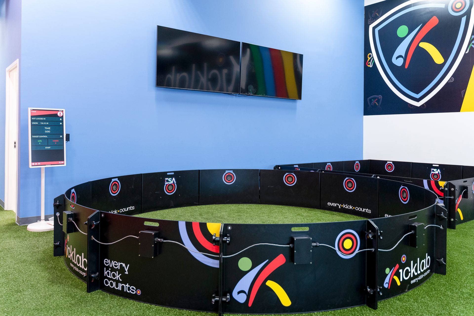 Indoor black-and-rainbow branded playpen on green turf against a light blue wall