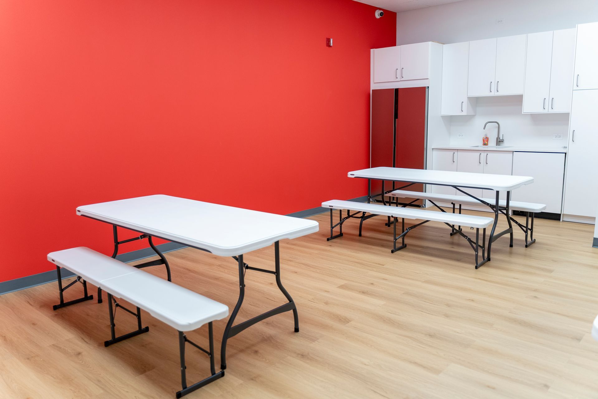 Empty room with red and white walls, folding tables and benches on a light wood floor.