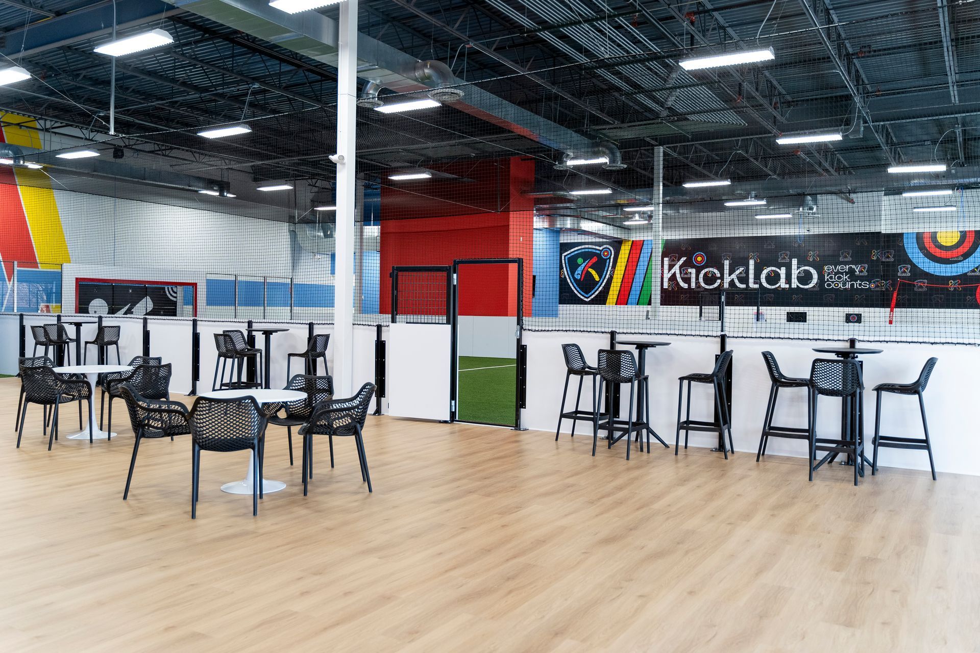 Open studio with tables and chairs on a wood floor, colorful wall mural, and industrial ceiling lights