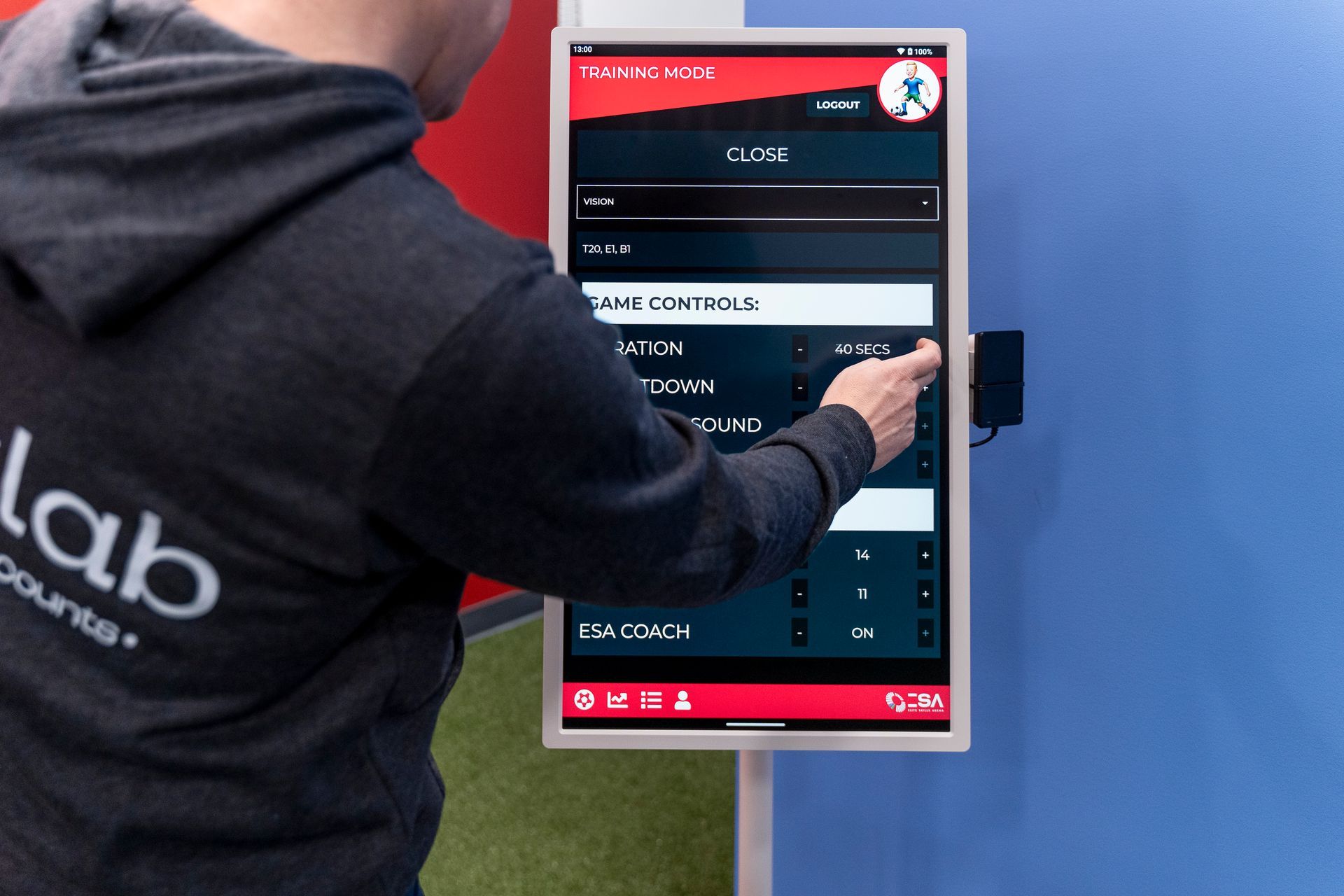 Person using a touchscreen payment kiosk outdoors, with a red interface on a blue wall.